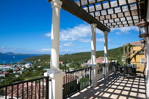 A balcony with a view of the sea, white columns, and a wooden pergola.