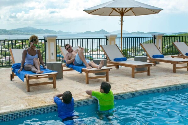 A poolside area with lounge chairs, a pool, and a view of the sea.