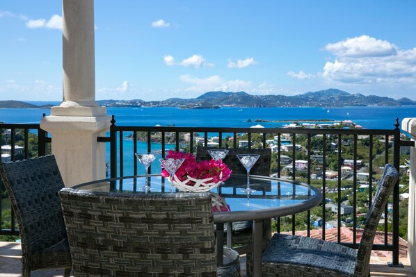 A balcony with wicker chairs, a glass table, and a vase of flowers.