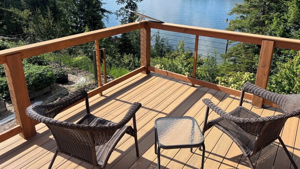 A wooden deck with wicker chairs and a small table, overlooking a lake with trees and a dock. - Carlin Bay Retreat on Lake Coeur d'Alene  (Harrison)