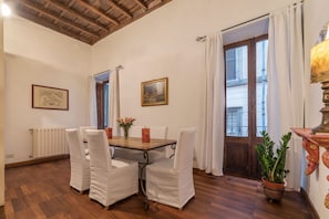 Un comedor con una mesa de madera, sillas blancas y una planta en maceta.