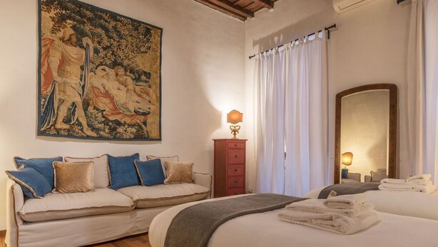 Une chambre d’hôtel avec une grande tapisserie, un canapé, un lit avec des serviettes, une commode et un miroir.