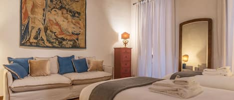 A hotel room with a large tapestry, a sofa, a bed with towels, a dresser, and a mirror.