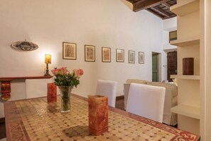 A dining area with a patterned table, white chairs, a vase with flowers, and framed artwork on the wall. - Unique opportunity to live in a Renaissance palace (Roma)