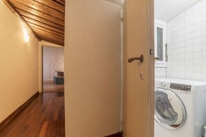 A laundry room with a washing machine, wooden flooring, and a door leading to another room. - Unique opportunity to live in a Renaissance palace (Roma)