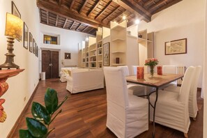 A spacious room with a wooden ceiling, white walls, and a dining area with a table and chairs. There are bookshelves and a door in the background. - Unique opportunity to live in a Renaissance palace (Roma)
