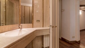 Une salle de bain avec un grand miroir, un lavabo et une porte donnant sur une autre pièce.
