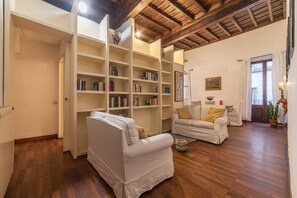 A spacious living room with wooden flooring, white sofas, and a large bookshelf filled with books. - Unique opportunity to live in a Renaissance palace (Roma)