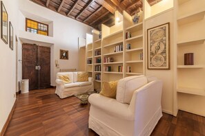 A cozy living room with a white sofa, wooden flooring, and a bookshelf filled with books. - Unique opportunity to live in a Renaissance palace (Roma)