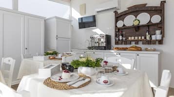 Una cocina luminosa y bien iluminada, con armarios blancos, una cafetera y un estante de madera rústica con platos y frascos.