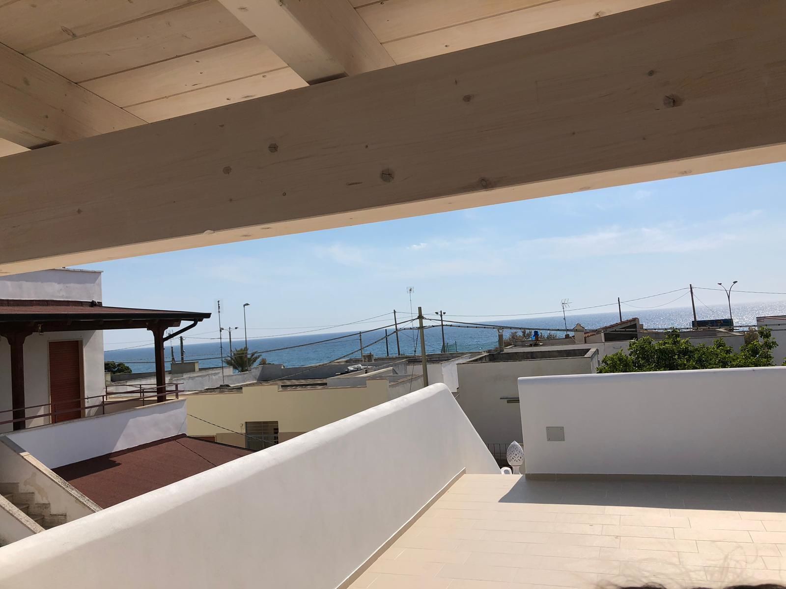 A rooftop terrace with a view of the sea and neighboring buildings.