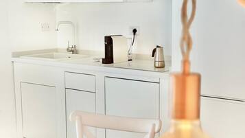 Una cocina moderna con armarios blancos, microondas, cafetera y una bombilla colgante.