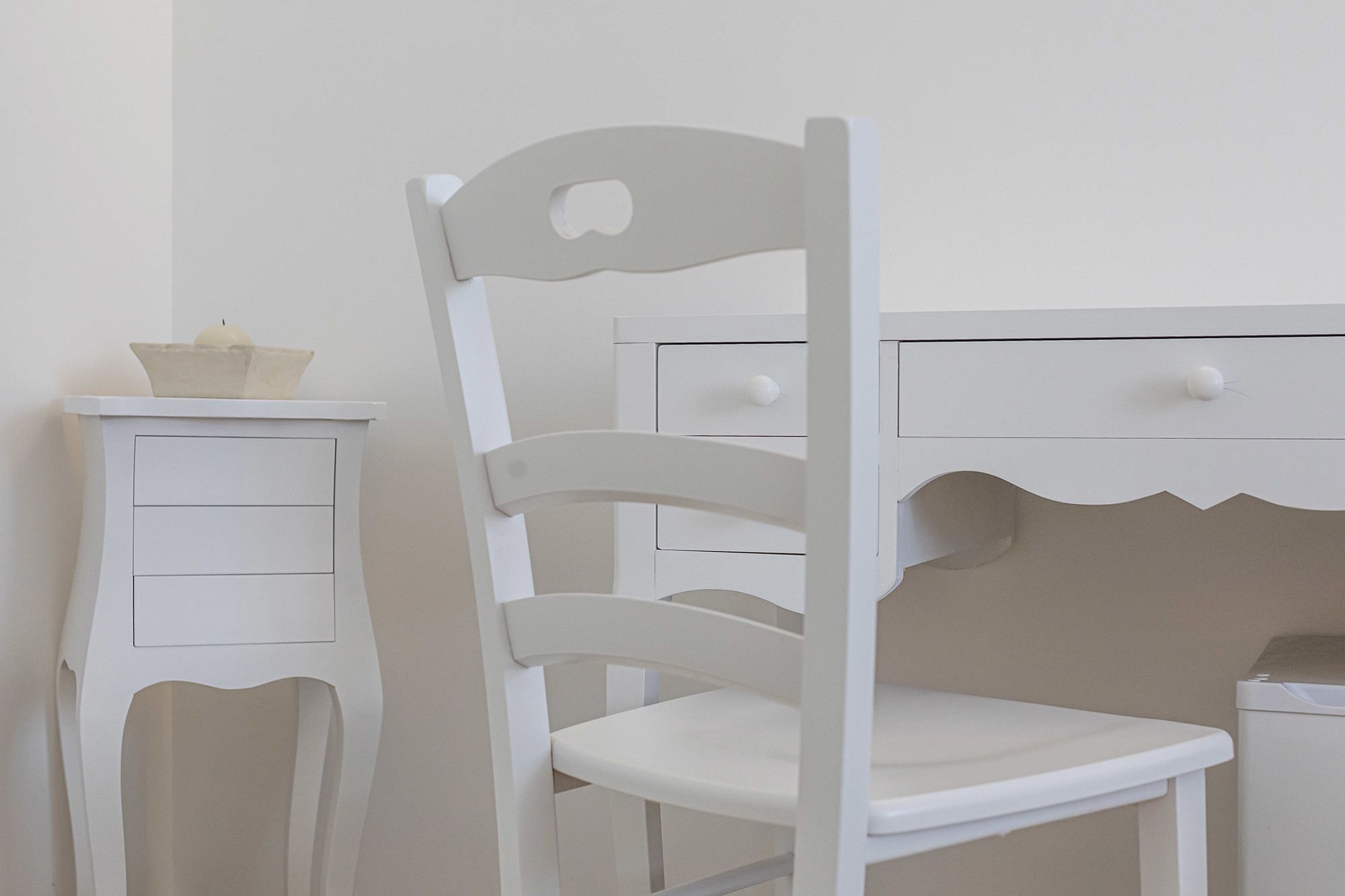 A white desk with a chair and a small cabinet.