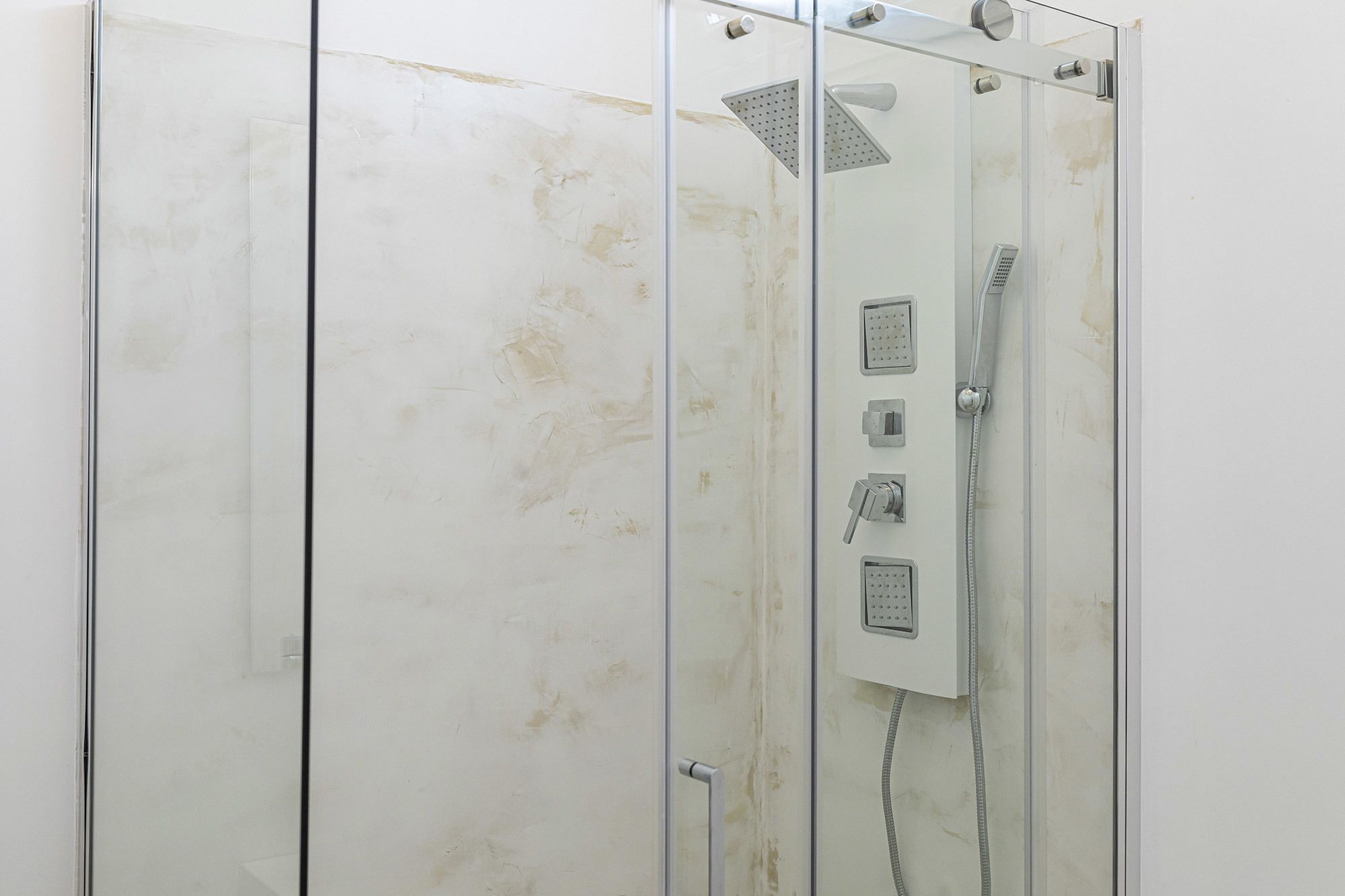 A glass-enclosed shower stall with a handheld showerhead and a wall-mounted control panel.