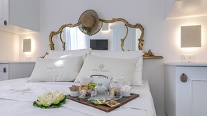 A neatly made bed with a tray of breakfast items, a decorative hat, and a mirror with an ornate frame. - Petra Bianca (Ugento)