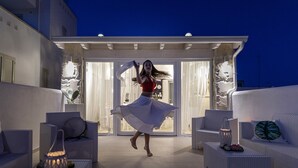 A woman in a red top and white skirt dancing on a balcony with white wicker furniture and a glass door leading to a bright interior. - Petra Bianca (Ugento)