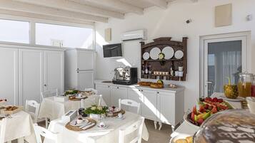 A bright, sunlit kitchen with white cabinetry, a coffee machine, and a fruit display.