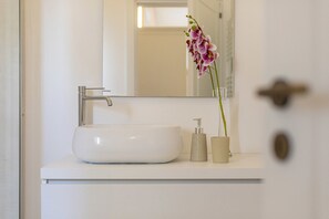 A bathroom with a white sink, a mirror, and a potted orchid. - Petra Bianca (Ugento)