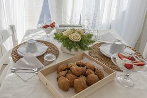 A dining table set with a variety of food items, including a bowl of bread rolls, a glass dessert with strawberries, and a vase with flowers. - Petra Bianca (Ugento)