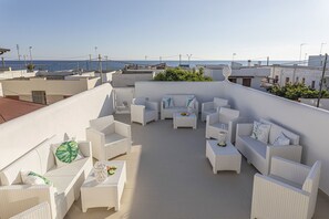 A rooftop terrace with white wicker furniture, a small table with a vase, and a view of the sea. - Petra Bianca (Ugento)
