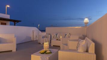 Terraza en la azotea con mobiliario de mimbre blanco, incluyendo sofás y sillones, dispuestos alrededor de mesas con adornos decorativos.