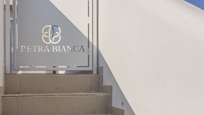 A sign with the text "PETRA BIANCA" and a logo, mounted on a white wall with steps leading up to it. - Petra Bianca (Ugento)