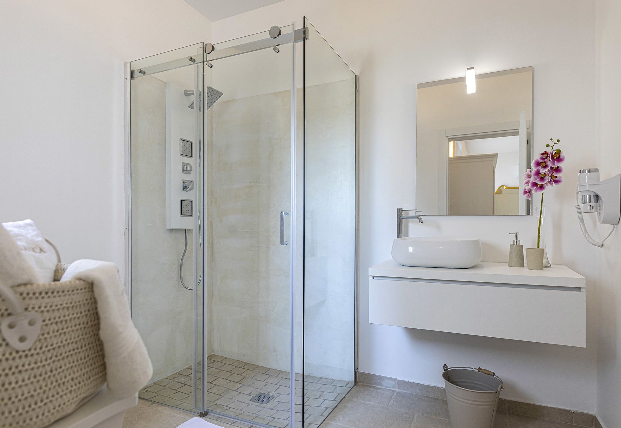 Un baño moderno con ducha envuelta en vidrio, un lavamanos blanco y un espejo sobre él.