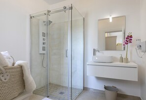 A modern bathroom with a glass-enclosed shower, a white sink, and a mirror above it. - Petra Bianca (Ugento)
