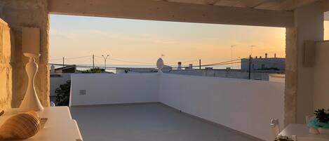 A spacious rooftop terrace with a clear view of the sea and city skyline during sunset.