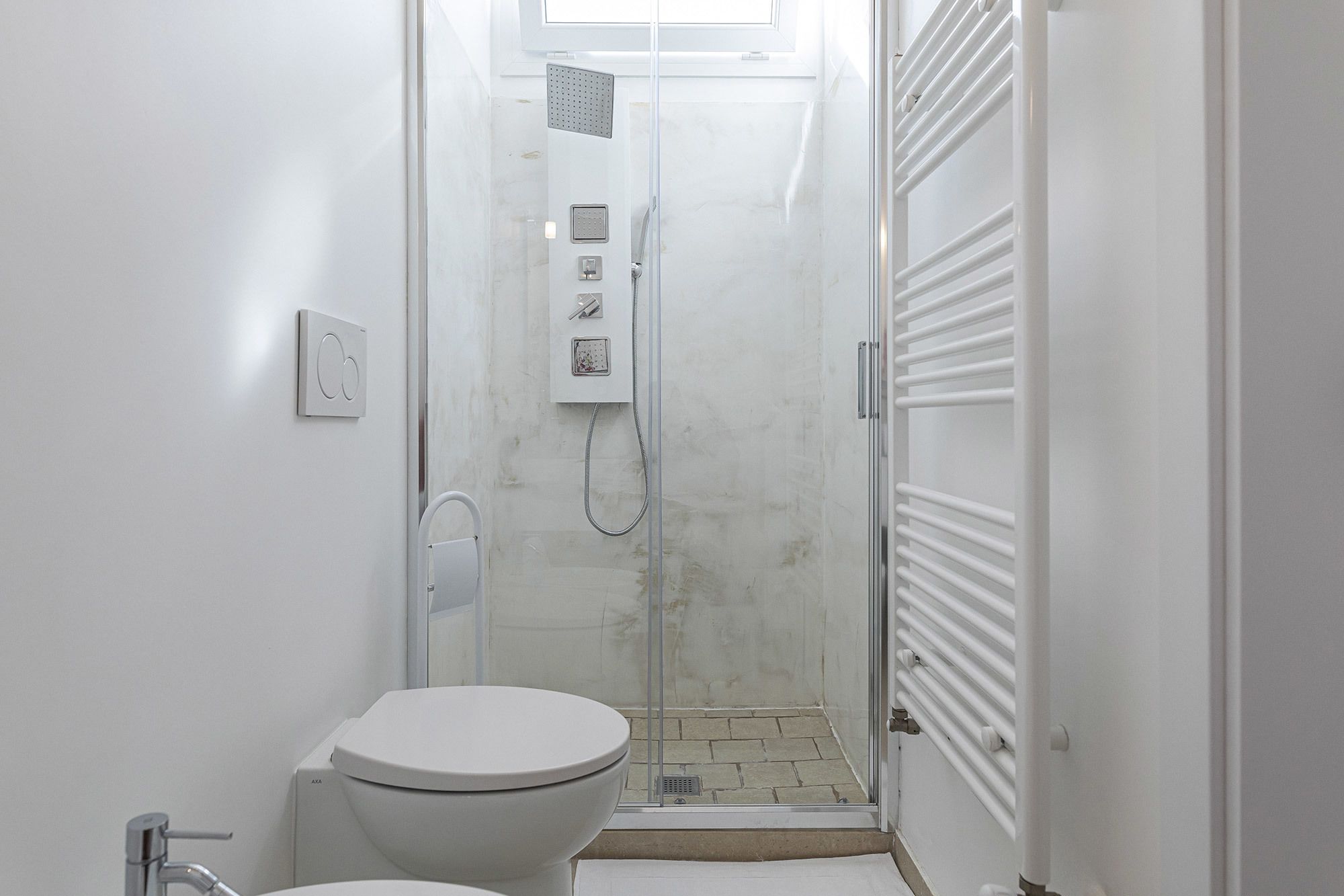 A small, modern bathroom with a toilet, a shower stall, and a radiator.