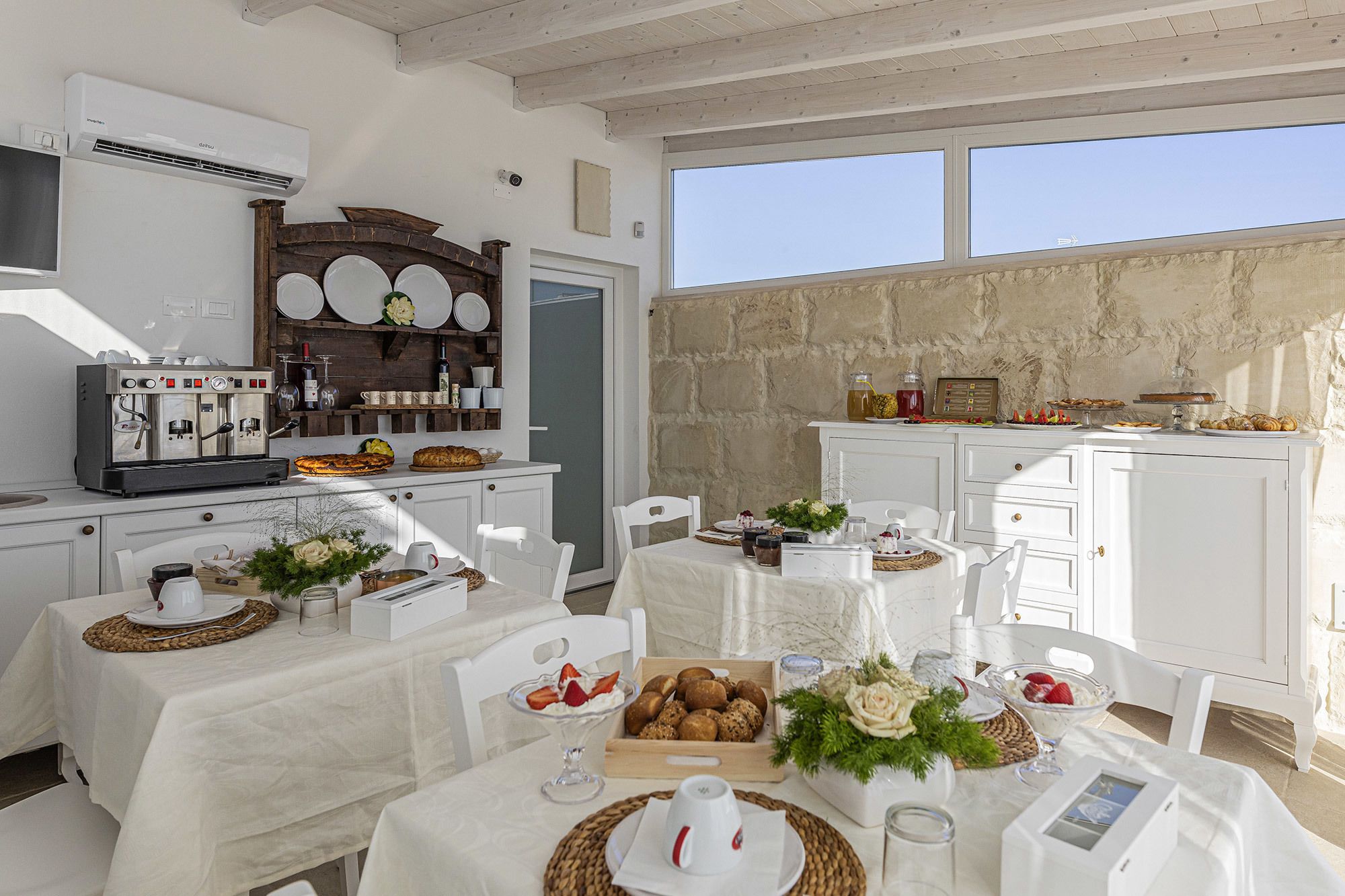 A dining area with white tables, a coffee machine, and a stone wall.