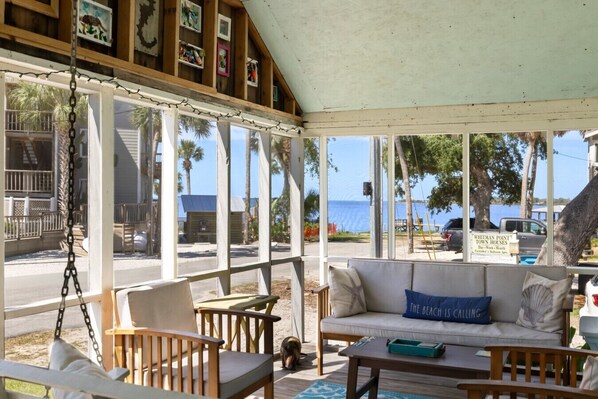Un área de estar al aire libre con techo y vistas a la playa y al océano, mobiliario de madera y un letrero que indica Whitman Point Town Houses.
