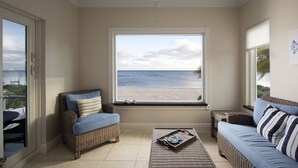 A room with a large window overlooking a beach, wicker furniture, and a ceiling fan.