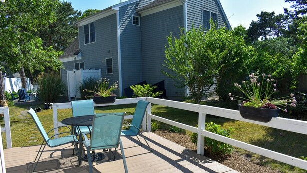 A deck with outdoor furniture, a white fence, and potted plants. - Charming 2-Bedroom Cottage Just 2/10 Mile from Sea Street Beach! (Dennis Port)
