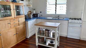 A kitchen with white cabinets, a wooden cabinet with glass doors, a microwave, a sink, a stove, and a rolling cart with pots. - Burrum Beach House-Waterfront-Private Jetty-2BR (Burrum Heads)