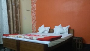 A neatly made bed with a floral bedspread and white pillows, a wooden headboard, and a small trash bin beside the bed. - Elation Guest House & Musafir Cafe (Ranikhet)
