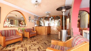A cozy living room with wooden furniture, a herringbone-patterned floor, and a large mirror. - Hotel Margarita (Puno)