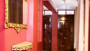 A hallway with a patterned wooden floor, a mirror with an ornate frame, and a red wall. - Hotel Margarita (Puno)
