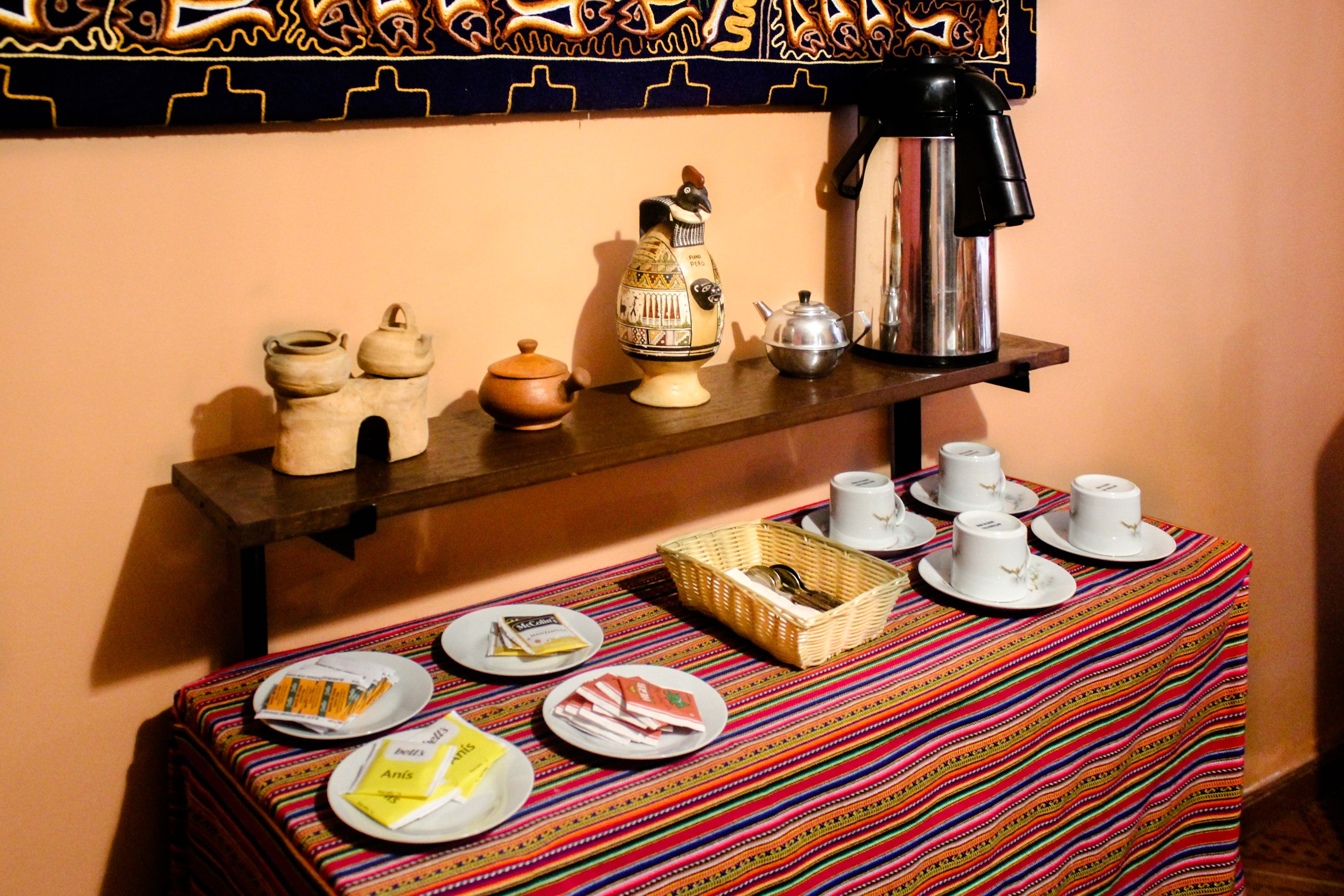 Una mesa con cafetera, tetera y diferentes tazas y platos para el desayuno.