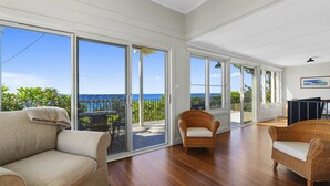 En rummelig stue med en stor skydedør, der fører ud til en balkon med havudsigt. Der er to fletstole og en sofa i stuen.