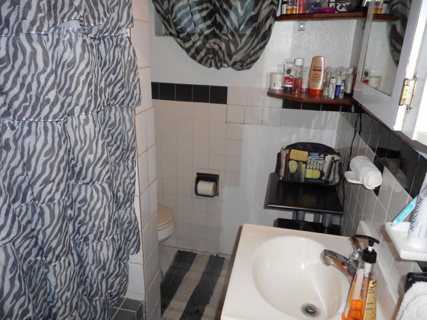 A bathroom with a zebra-striped shower curtain, a white sink, a mirror, and toiletries on a shelf.