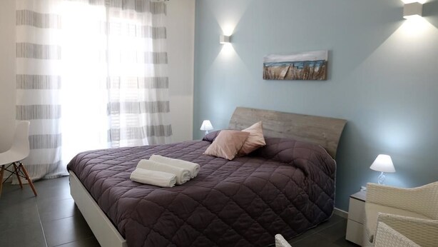 A bedroom with a large bed, a nightstand, a chair, and a painting on the wall. - B&B Al Porticciolo (Marsala)