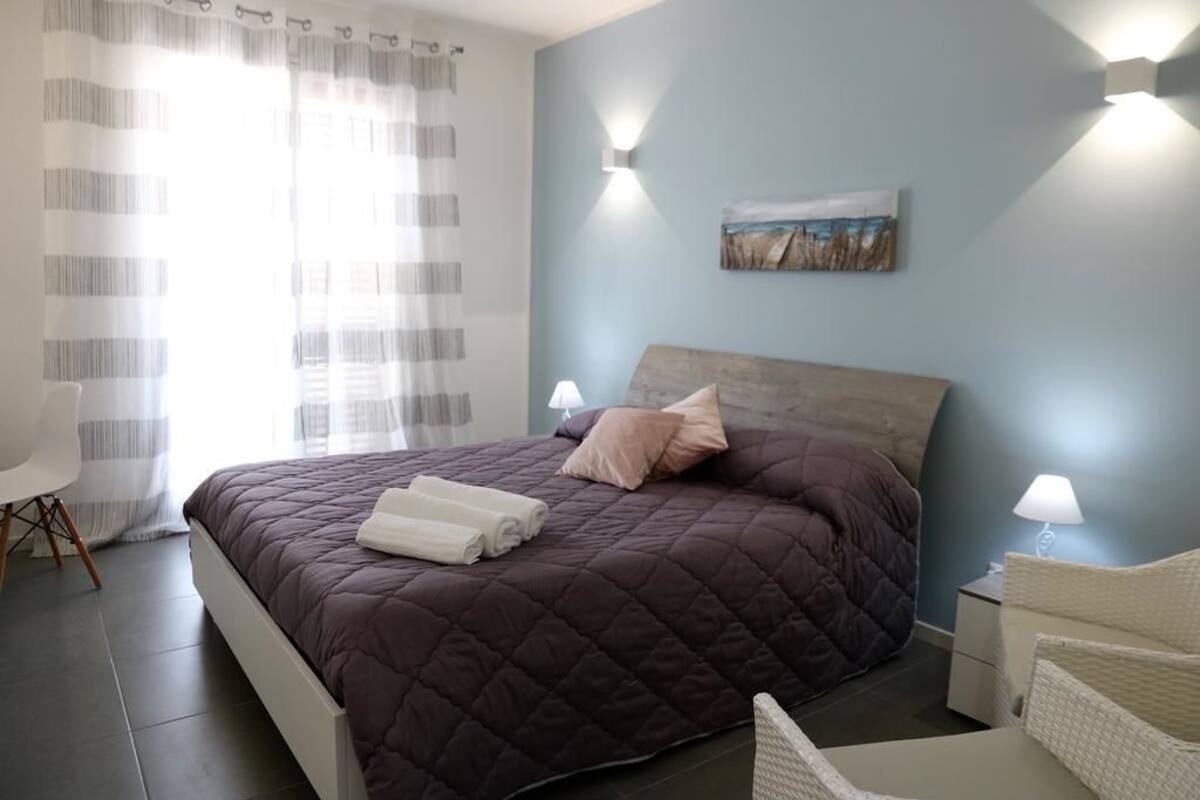 Quarto com uma cama grande, mesa de cabeceira, cadeira e um quadro na parede.