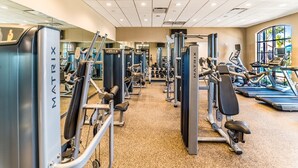 A gym with various exercise machines, a mirrored wall, and a window with a view of palm trees. - Cost-effective!!! 9Br/6Ba Pool Villa with lake view,Near Disney (Kissimmee)
