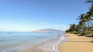 A beach with clear water, a sandy shore, and palm trees. - Aloha Villas # 2, Steps to Beach, Close to Golf & (Kihei)