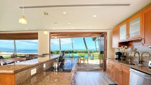 A modern kitchen with a granite countertop, wooden cabinets, and a view of the ocean. - Aloha Villas # 2, Steps to Beach, Close to Golf & (Kihei)