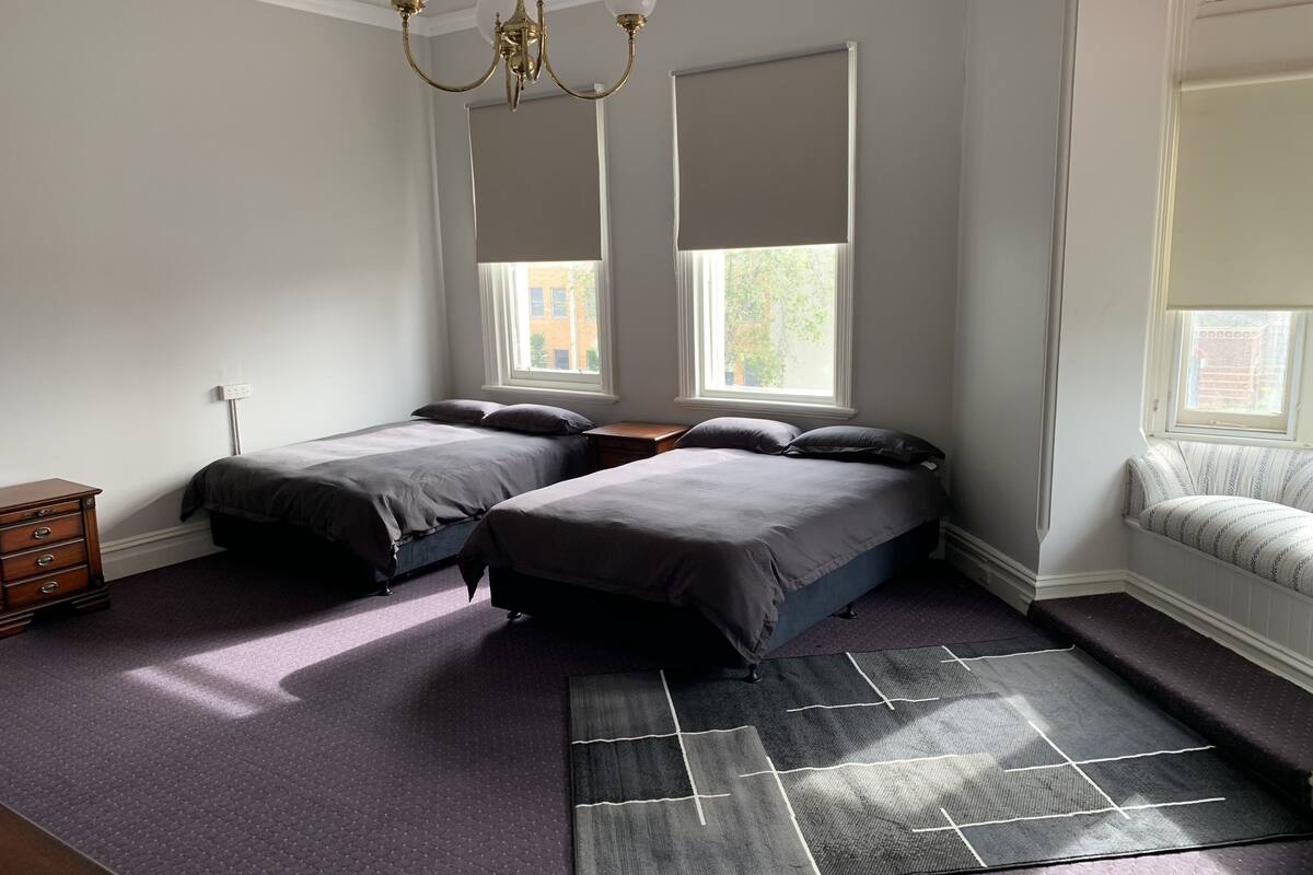 A bedroom with two beds, a dresser, a rug, and a window with blinds.