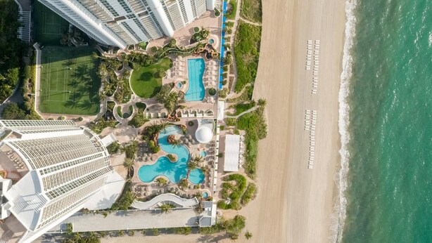 Oversigtsbillede af et resort med flere swimmingpools, en strand og høje bygninger.