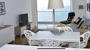 A modern living room with a dining table, white chairs, a sofa, and a television. - Xenon urban apartments (Maputo)