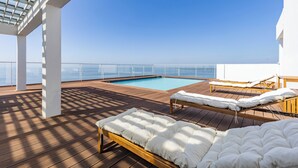 A sunlit outdoor deck with a pool, lounge chairs, and a wooden bed. - Xenon urban apartments (Maputo)